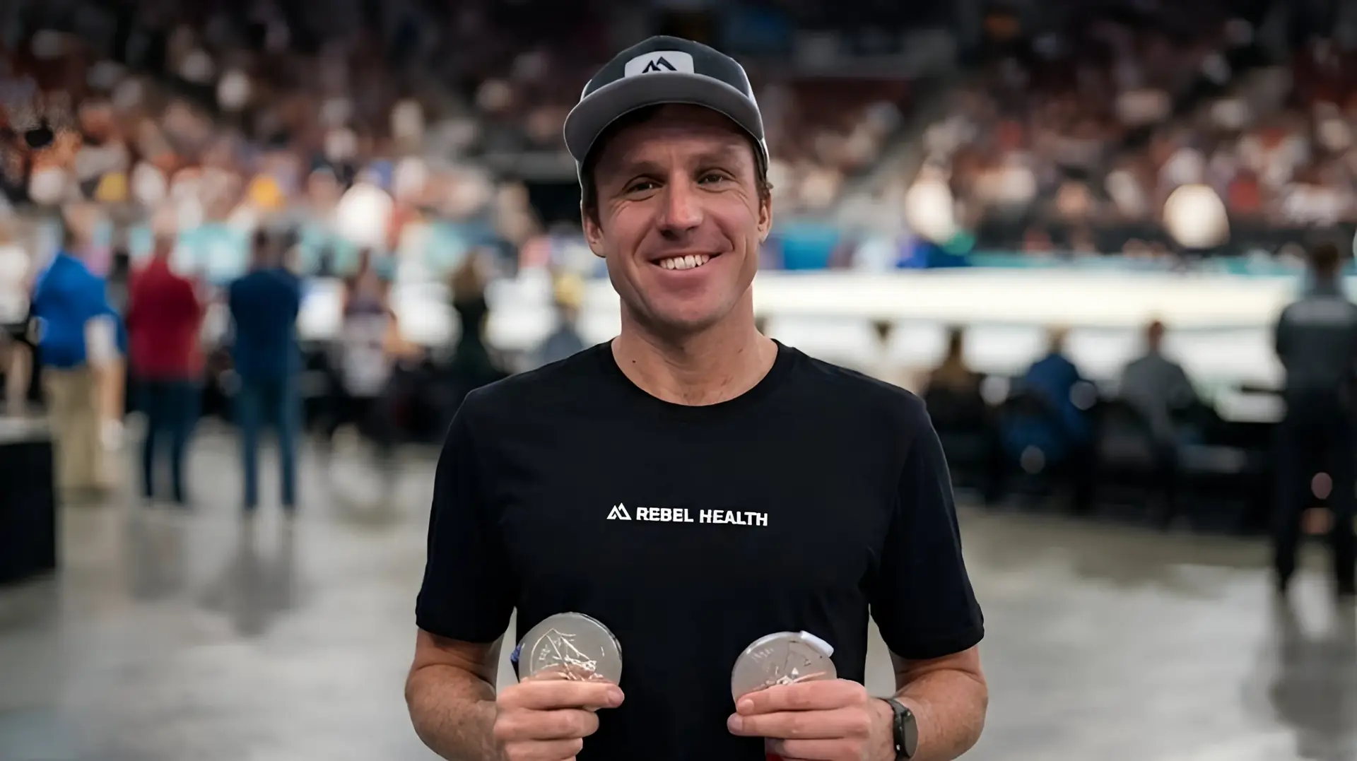 Morgan Pearson holding two Olympic silver medals in a Rebel Health shirt